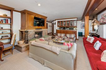 The inviting living area of Plaza Lodge 3 Bedroom Gold Unit 2, featuring a stone fireplace, comfortable seating, and a well-appointed wet bar, offers a perfect blend of rustic charm and modern convenience.