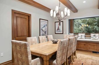 A dining room table with six chairs in a home with a large window looking out at the snowy trees