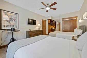 A cozy bedroom at The Charter G135 featuring two queen beds, a dresser with a TV, a Beaver Creek ski poster, and a built-in wet bar.
