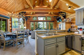 A spacious kitchen and dining area in a log cabin with a view of the forest and mountains.
