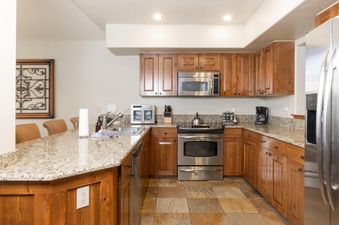 The kitchen at Villa at Mountain Thunder features a spacious granite countertop, wood cabinetry, and stainless steel appliances, including a microwave, oven, and refrigerator.