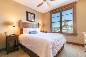A bedroom with a king bed, two nightstands with lamps, and a window with a view of a snow-covered town.