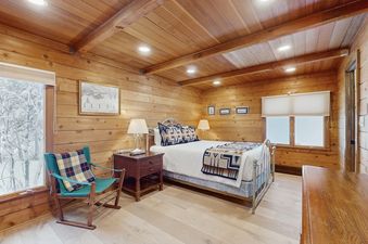 A cozy bedroom in Wood Road House with wooden walls and a window displaying a snowy outdoor view.