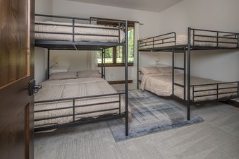 A cozy bedroom features two black metal bunk beds, each with beige bedding, on a light-colored carpet with a blue rug between the beds.