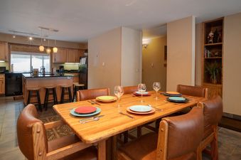 A spacious dining area with a wooden table set for six people, leading into a well-equipped kitchen with a large island and bar stools.