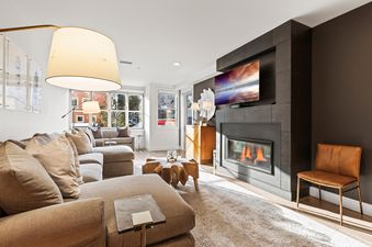 The Rio Grande 203 204 living room, featuring a cozy L-shaped sofa, a unique wooden coffee table, a modern fireplace with a mounted TV, and large windows with outdoor views.