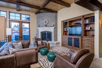 A living room with a large fireplace, a leather couch and chairs, a built-in entertainment center with a TV, and a zebra-print rug.