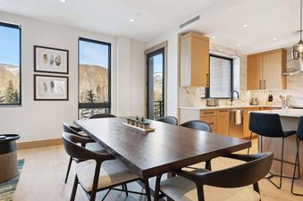 The dining room in One Riverfront Condo 203 features a large, dark wood table with six chairs, a view of the mountains, and a set of potted plants in the center.