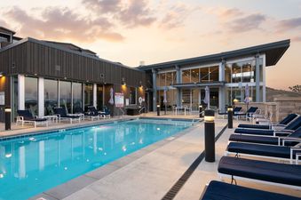 A modern outdoor pool area at Apex 208 with lounge chairs and a building with large windows under a twilight sky.