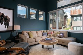 Cozy and stylishly decorated lounge area at Konik Chalet with a beige sectional sofa, rustic wooden details, and large windows.