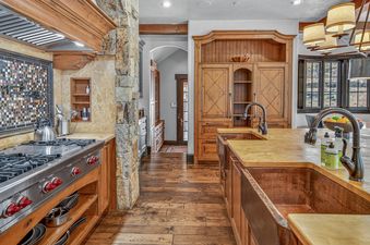 A rustic-chic kitchen with rich wood cabinetry, a double copper sink in the island, a stainless steel stove, and a mosaic tile backsplash.