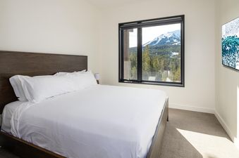 A bedroom in Moonlight Basin 204 Lakelodge with a large window offering mountain views and a TV on the wall.
