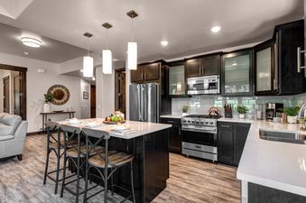 The kitchen in Blackstone 13th Green is well-equipped with stainless steel appliances, a large island with seating, and beautiful wood cabinets.