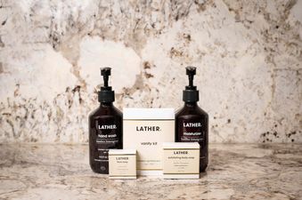 A Lather vanity kit featuring two pump bottles of hand wash and moisturizer, along with two boxed soaps, all displayed on a marble countertop.