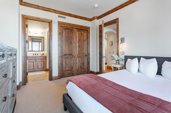 The bedroom in Grand Lodge Three Bedroom 301 features a comfortable bed with a red quilted throw blanket, a large closet, and a window providing natural light.