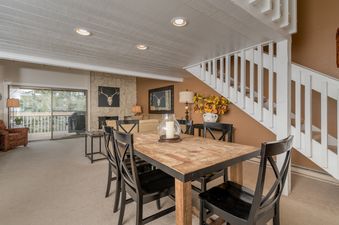 A spacious dining room with a wooden table and chairs, a fireplace, and a view of a wooded area.