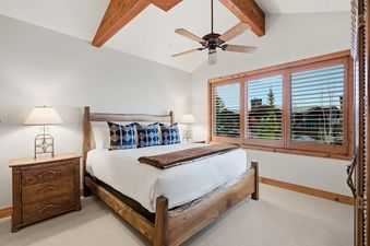 A king bedroom in Summit View Lodge at Deer Valley with rustic wooden furniture, a ceiling fan, and a large window with wooden shutters.