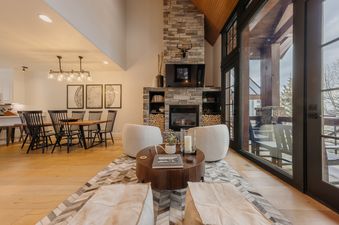 A cozy, modern living room at the Campfire Cabin at See Forever featuring a large stone fireplace, plush armchairs, and floor-to-ceiling windows.