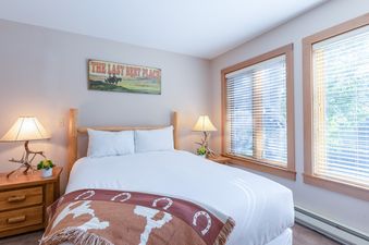 A cozy bedroom in Rendezvous D1 featuring a rustic wooden bed, matching antler lamps, and two windows with blinds.