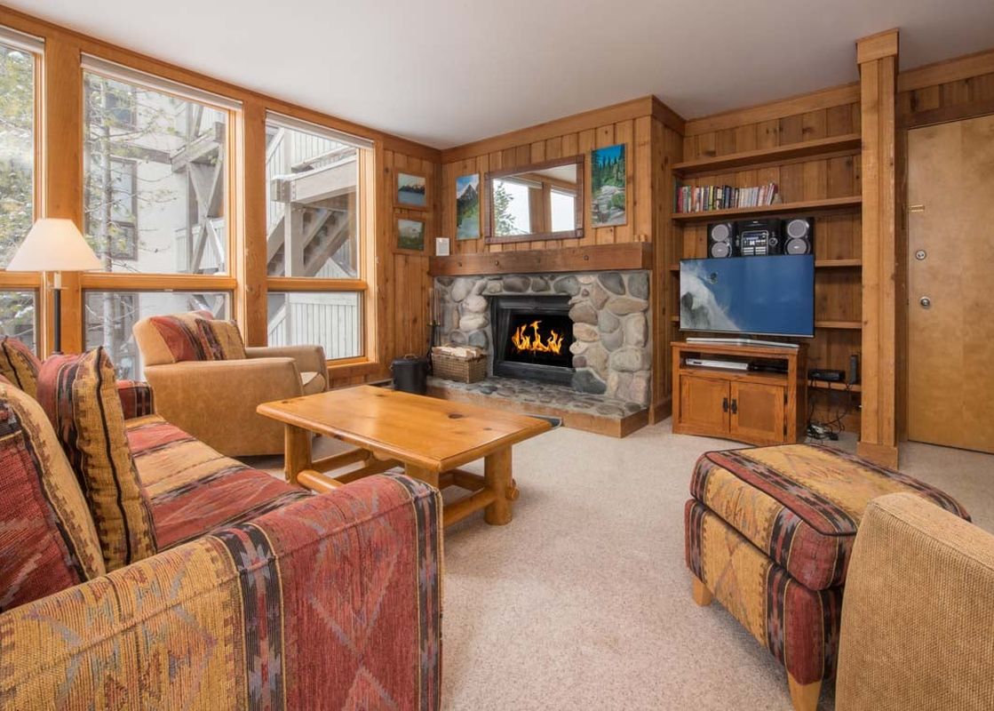 Cozy living area in Nez Perce C4 with a stone fireplace, pattern sofas, wooden paneling, and large windows.