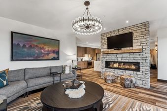 The Hot Toddy's spacious living room features a grey sectional sofa, a large artwork, a stone fireplace with a TV, and an open view to the modern kitchen.