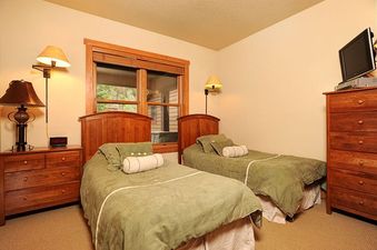 A cozy bedroom in Redhawk Townhome 3 Bedroom featuring two single beds with green bedding, wooden headboards, and bedside tables with lamps.