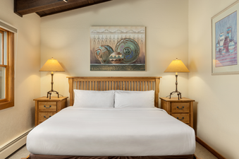 A cozy bedroom with a king-size bed, two nightstands with lamps, a painting above the bed, and a window.