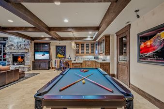 A luxury games room featuring a pool table, wet bar, and stone fireplace at Mountains Edge.