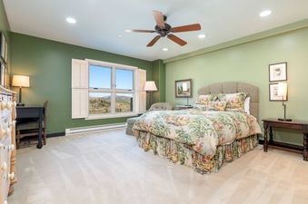 A master bedroom at Peaks Penthouse 846, featuring a large bed with a floral comforter, a ceiling fan, and a desk, all set against sage green walls and a large window overlooking snowy mountains.