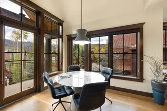 A modern dining area at On Trails Edge with a round marble-top table, four black chairs, and large windows offering panoramic mountain and autumn views.