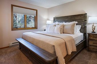 A cozy bedroom at The Ranch at Steamboat RA216 with a large bed, rustic wooden furniture, and a window offering views of evergreen trees.