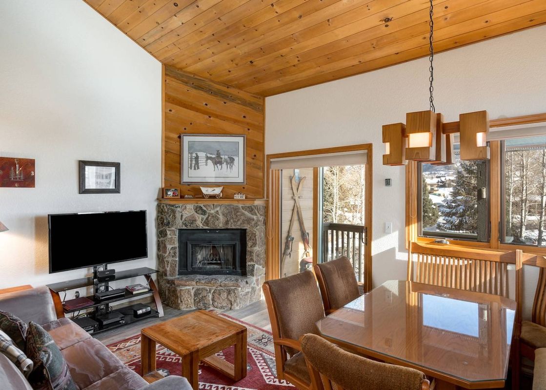 The Pines Condominiums A304's living and dining room with a stone fireplace and views of a snowy landscape.