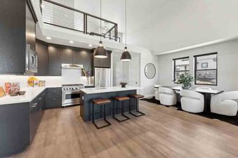A modern kitchen with white countertops and dark cabinets, a large island with four bar stools and a dining area with white chairs.
