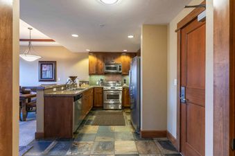 A kitchen with stainless steel appliances and wood cabinets, a dining area to the left, and a door to the hallway on the right.