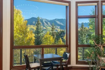Dining table and chairs near large windows showcasing a stunning mountain and autumn forest view.
