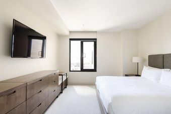 White bedroom with a queen-sized bed, a dresser, and a flat-screen television.