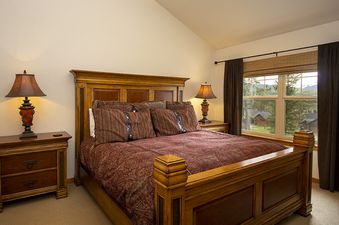 A cozy bedroom with a large wooden bed, two bedside tables with lamps, and a window offering a view of a mountainous landscape.