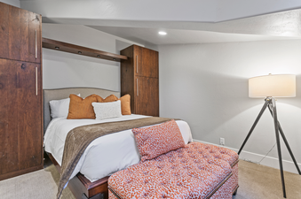 A bedroom in the Lodges at Deer Valley 2 Bedroom Suite with a king-size bed, a brown throw blanket and an orange throw pillow on the bed, an ottoman, a floor lamp, and a wall of closet doors.