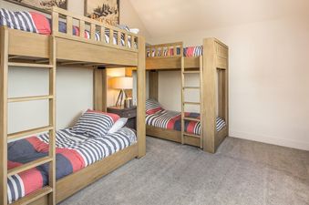 A bunk bed room with a grey carpeted floor and two sets of bunk beds. The lower beds are made and both beds have a white and blue striped comforter.