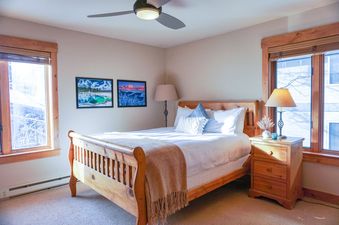 A cozy bedroom in Rendezvous D3 with a wooden bed, natural light, and a ceiling fan.