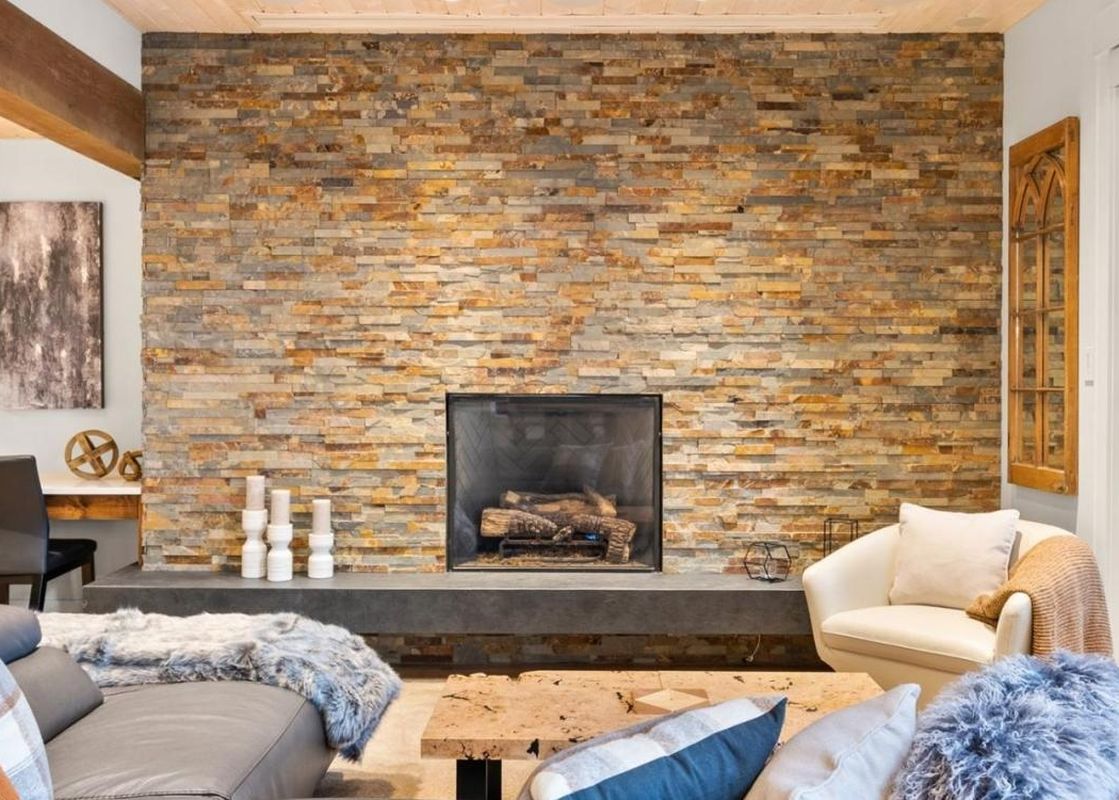 The inviting living area of Northern Lights 42 features a prominent stone fireplace, comfortable seating, and a large sliding glass door leading to a snowy outdoor view.