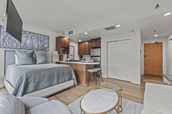 A modern studio apartment at Galleria 307 with a bed, kitchenette, and living area in an open-concept layout.