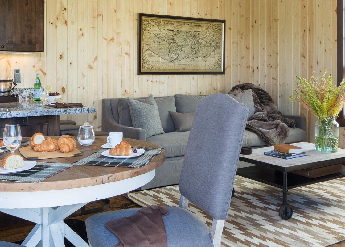 An inviting open-concept living area with a dining table set for breakfast, an adjacent lounge with a sofa, and a modern kitchen, all bathed in natural light.