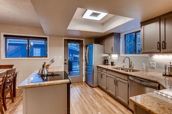 The kitchen at High Street Retreat features light wood floors, grey cabinets, and granite countertops.