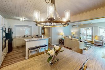 The open-concept living area of Dulany 105 features a full kitchen, a comfortable lounge area, and a rustic dining table illuminated by a stylish chandelier.