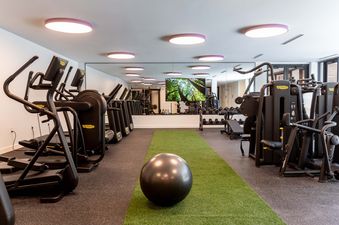 The fitness center at Founders Place 1403 is equipped with Technogym cardio machines, a green artificial turf area with an exercise ball, mirrored walls, and a large screen displaying a forest view.
