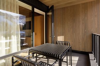 A private outdoor terrace featuring a black metal dining set, with large glass sliding doors reflecting snow-covered mountains.
