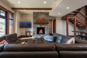 A cozy living room at Granby Ranch Lodge featuring a leather sectional, stone fireplace, and rustic wooden details.