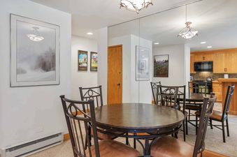 A round dining table with dark bronze finish and matching chairs with brown leather seats in the dining area of The Charter E0105.