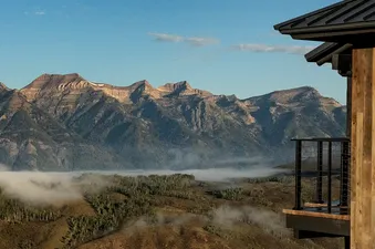 A modern suite with a wooden exterior and a balcony overlooking a vast mountain range with a misty valley.
